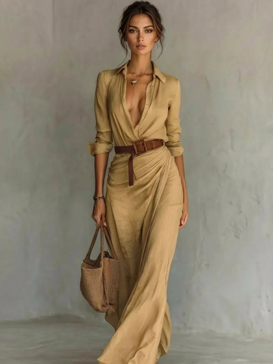 Woman wearing a beige dress with a brown belt and holding a matching handbag against a neutral background.